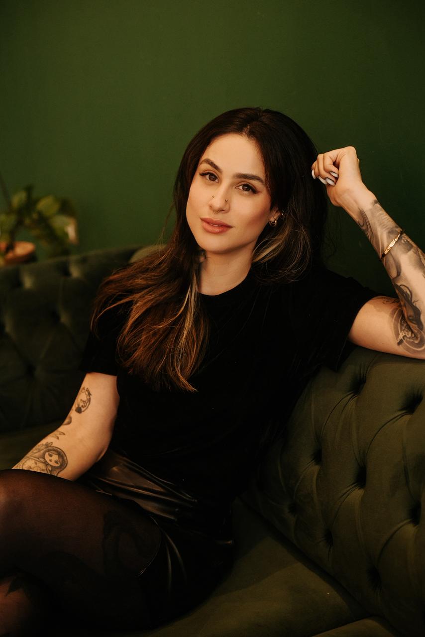 Retrato da Fabiana Dias sentada em um sofá de veludo verde